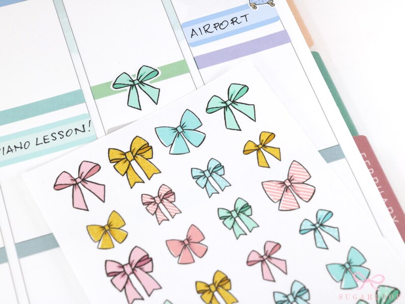 May include: A sheet of colorful bow stickers with a variety of colors including pink, yellow, blue, and green. The stickers are arranged in rows on a white background. The text "PIANO LESSON!" is written on the sheet.