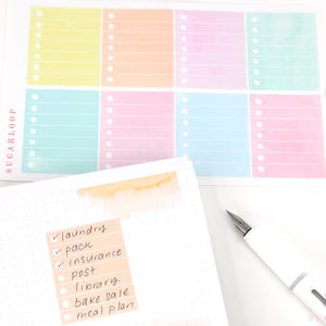 May include: A sheet of colorful pastel checklist stickers with a handwritten to-do list on a dotted notebook page. The list includes laundry, pack, insurance, post, library, bake sale, and meal plan.