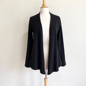 May include: A black open-front cardigan with long sleeves, displayed on a mannequin. The cardigan has a flowing, flared design at the hem. The garment is made of a soft, draping fabric.