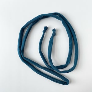 May include: A teal-colored fabric strap with two knotted ends. The strap is looped and appears to be made of a soft, flexible material. The background is plain white.
