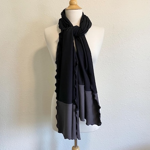 May include: A black and gray scarf with a ruffled edge. The scarf is draped around a mannequin's neck.