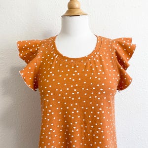 May include: A rust-colored top with white polka dots and ruffled short sleeves.