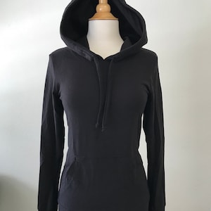 May include: A black hooded sweatshirt with long sleeves and a front pocket. The sweatshirt is displayed on a mannequin against a white background. The hood has a drawstring.