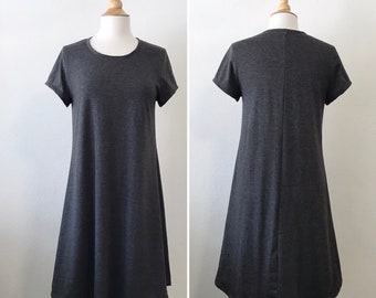 May include: A dark gray short-sleeved dress with a round neckline and a flared A-line silhouette. The garment is displayed on a mannequin, showing both the front and back views of the solid-colored, knee-length jersey knit fabric.