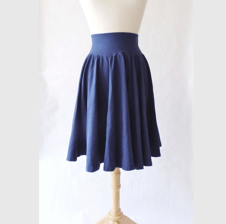 May include: A solid navy blue knee-length skirt featuring a wide, high-waisted elasticized waistband and a full, pleated silhouette that flares outward from the waist, displayed on a mannequin against a plain white background.
