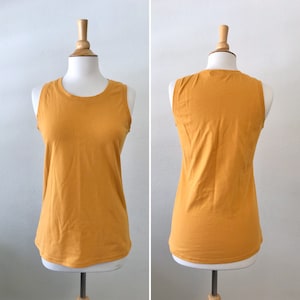 May include: A mustard yellow sleeveless tank top on a mannequin. The tank top has a scoop neck and a relaxed fit.