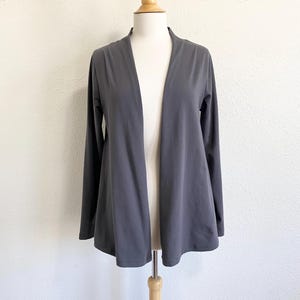 May include: A charcoal gray open-front cardigan with long sleeves. The lightweight fabric drapes over a mannequin, showcasing the garment's relaxed fit. The cardigan has a simple, minimalist design, suitable for layering.