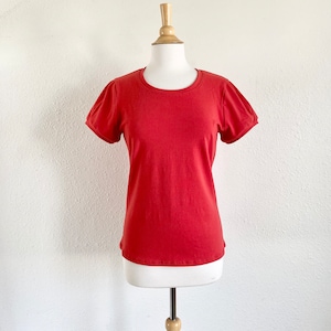 May include: A solid red t-shirt with short, puffed sleeves. The round-neck top is displayed on a white mannequin. The shirt is made of a soft material and is suitable for casual wear.