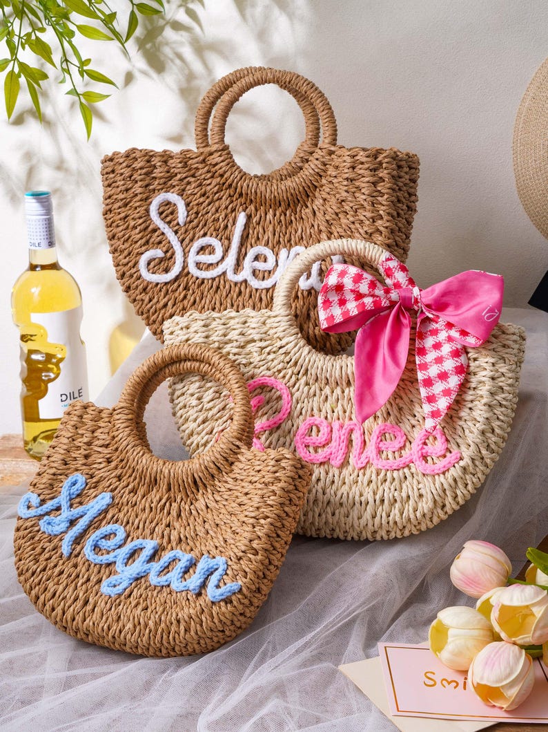 May include: Three woven straw tote bags with round handles. The back bag is brown with the white embroidered name "Selena". The middle bag is light beige with the pink embroidered name "Renee" and a pink gingham bow. The front bag is brown with the light blue embroidered name "Megan".