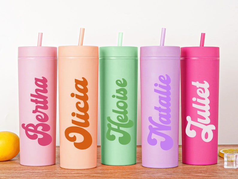 May include: Five colorful tumblers with lids and straws, each in a different pastel shade: pink, peach, green, lavender, and hot pink. Each tumbler has a name printed on it in a retro font: Bertha, Olicia, Heloise, Natalie, and Juliet.