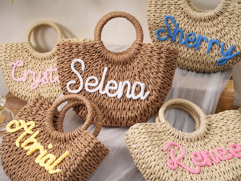 May include: A collection of five woven straw handbags with round handles, each featuring a personalized name embroidered in cursive yarn. The names displayed on the bags are Crystal in pink, Selena in white, Sherry in blue, Alrial in yellow, and Renee in pink.