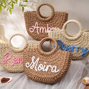 May include: Four woven straw handbags with round handles, each featuring a personalized name embroidered in cursive yarn. The names Amber, Sherry, Ren, and Moira are displayed in pink, blue, and white colors on the front of the textured bags.