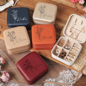 Peut inclure: Plusieurs bo&icirc;tes &agrave; bijoux carr&eacute;es personnalis&eacute;es, de couleurs vari&eacute;es : bleu marine, beige, orange et bordeaux. Chaque bo&icirc;te est orn&eacute;e d'un motif floral et d'un nom. Une bo&icirc;te est ouverte, r&eacute;v&eacute;lant des compartiments.