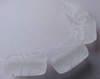 May include: Close-up of a strand of white, rectangular beads with a frosted finish. Each bead features a delicate, swirling white pattern. The beads are strung together on a thin, clear cord, suggesting jewelry making.