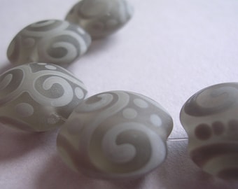 May include: A series of four rounded, translucent grey beads arranged in a curved line. Each bead features a matte, opaque white pattern consisting of swirling lines and small circular dots that contrast against the smooth, semi-transparent grey surface.