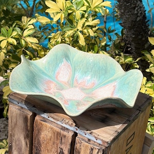 May include: A ceramic bowl with a wavy, organic rim featuring a blended glaze of soft mint green, pale pink, and creamy white tones. The bowl has a shallow, wide basin with a smooth, glossy finish that highlights the swirling color patterns.