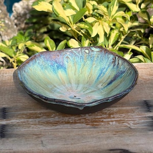 May include: A shallow ceramic bowl with an irregular, wavy rim. The interior features a glossy glaze with blended shades of turquoise, teal, and pale yellow, while the exterior and base are finished in a solid, dark matte brown glaze.