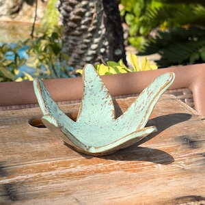 May include: A handcrafted, star-shaped bowl with a distressed, light turquoise finish. The bowl has a rustic, weathered appearance with visible wood grain and a natural, earthy aesthetic. The bowl is sitting on a wooden surface.