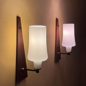 Puede incluir: Dos lámparas de pared con bases de madera y pantallas de vidrio blanco esmerilado. Las lámparas tienen un diseño moderno de mediados de siglo.