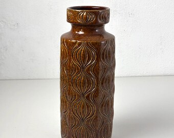 May include: A brown ceramic vase with a textured, repeating pattern. The vase has a cylindrical body and a slightly flared top with a decorative band. The overall height is approximately 10 inches.