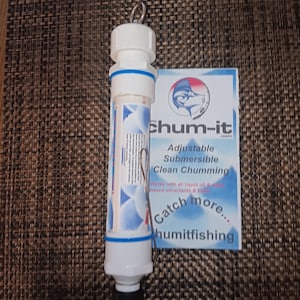 Puede incluir: Un dispensador de cebo de plástico blanco con una banda azul y una tapa negra. El dispensador tiene un anillo de metal en la parte superior y un clip de metal unido al lateral. El dispensador está etiquetado como "chum-it" y "Adjustable Submersible Clean Chumming". La etiqueta también dice "Works with all liquid oil & water based attractants & baits" y "Catch more... humitfishing".