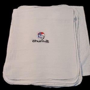 Puede incluir: Una pila de toallas de cocina de algodón blanco con un logotipo que dice "chum-it" con un gráfico de pescado en un círculo.