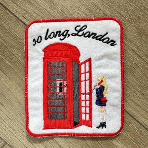 May include: Embroidered patch featuring a red London telephone booth with an open door. A person in a blue coat is on the phone. The text "so long, London" is arched above the booth, all on a white background with a red border.