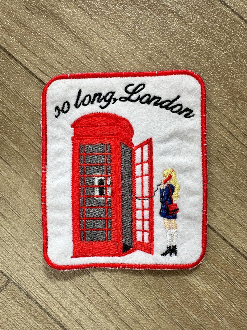 May include: Embroidered patch featuring a red London telephone booth with an open door. A person in a blue coat is on the phone. The text "so long, London" is arched above the booth, all on a white background with a red border.