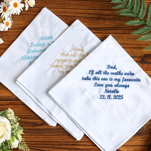 May include: Three white handkerchiefs with embroidered text in teal, gold, and blue. The handkerchiefs have text that reads "Mum Today a Tomorrow Always", "Dad, For all the support, and thank you", and "Dad, Of all the walks we've take this one is my favourite Love you always Natalie 22.11.2025".
