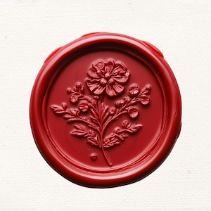 May include: A red wax seal with a floral design. The seal features a raised design of a flower with leaves and stems.