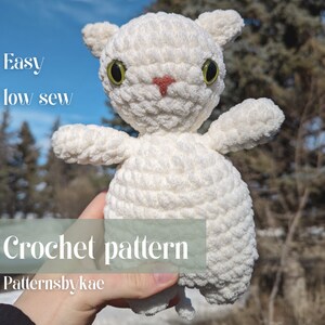 Könnte beinhalten: Weißes gehäkeltes Plüschtier mit grünen Augen und einer rosa Nase. Das Spielzeug wird in einer Hand gehalten und der Text "Easy low sew Crochet pattern Patternsbykae" ist auf dem Bild zu sehen.