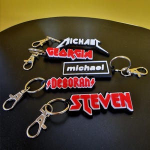 May include: A collection of keyrings featuring names in different fonts and colours. Names include "Michael", "Georgia", "michael", "Deborah", and "Steven". Each keyring has a silver clasp and ring.