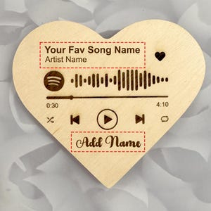 Op de afbeelding: Een hartvormige houten plaat met een Spotify-achtige muziekafbeelding. Het ontwerp bevat een afspeelknop, een golfvorm van een nummer en de tekst "Your Fav Song Name", "Artist Name" en "Add Name".