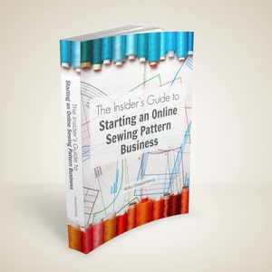 May include: A book titled "The Insider's Guide to Starting an Online Sewing Pattern Business" with a white cover and colorful spools of thread. The book's spine displays the title and author's name. Sewing patterns are visible.