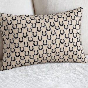 Horseshoe lumbar pillow cover on white bed, navy beige throw pillow, preppy equestrian decor for bedroom, horse pillow accent