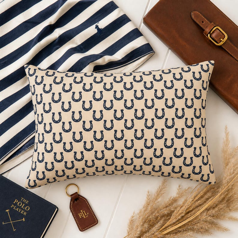 Preppy equestrian decor flat lay with horseshoe lumbar pillow, striped fabric and leather accessories, western home decor style