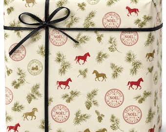 Puede incluir: Una caja de regalo rectangular envuelta en papel color crema con un patrón de caballos rojos y dorados, ramas de pino verdes y sellos rojos circulares que dicen NOËL POST. La caja está atada con una cinta negra fina en forma de lazo.