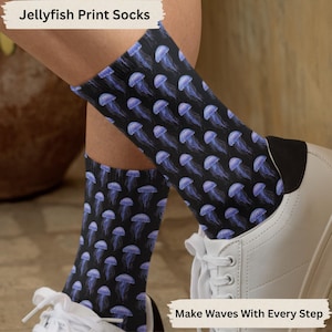 May include: A pair of black socks with a jellyfish print. The socks feature a repeating pattern of blue jellyfish on a black background. The text "Make Waves With Every Step" is printed on the bottom of the image.