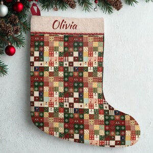 May include: A festive Christmas stocking with a patchwork design in red, green, and cream. The stocking features various festive patterns, including snowmen, snowflakes, and candy canes. The name "Olivia" is embroidered on the top.