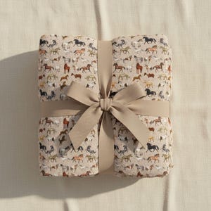 Folded beige horse plush blanket tied with ribbon, velveteen throw blanket gift for horse lovers, equestrian gift idea, western decor blanket, soft plush cozy throw, horse girl birthday gift, Christmas horse gift, farmhouse neutral blanket, horse themed home decor, country style throw blanket, luxury soft bedding accessory, aesthetic horse pattern, cozy comfort gift, western home accent, horse lover present