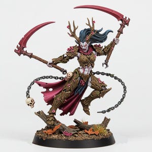 Peut inclure: Figurine miniature fantastique d'une guerrière avec des bois, tenant deux faux rouges. Elle porte une armure avec des accents floraux et une cape rouge. Une chaîne avec un crâne pend à sa taille.
