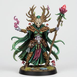 Peut inclure: Figurine miniature d'un esprit de la forêt, ornée de bois, d'un masque de crâne et de robes vertes fluides. La figurine tient un bâton surmonté d'un cristal rouge et d'une volute d'énergie rose. Des champignons miniatures sont à la base.