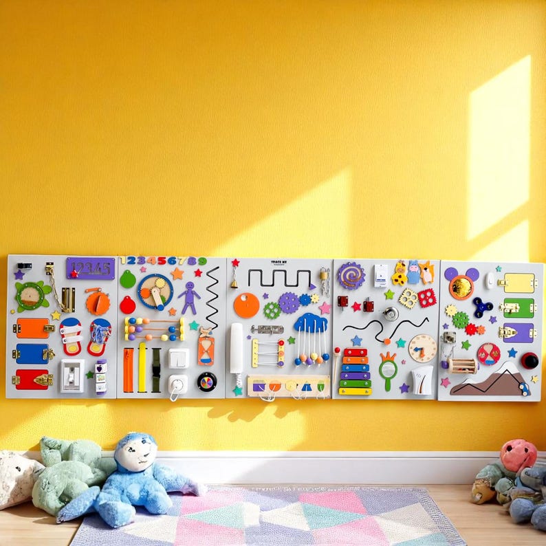 May include: A large, multi-panel sensory board for children, mounted on a yellow wall. The gray panels feature various interactive elements like latches, gears, beads, and shapes in bright colors. A xylophone and clock are also included.