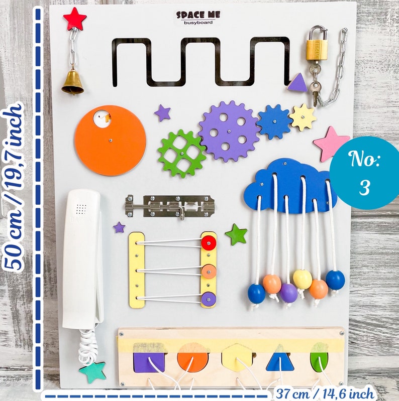 May include: A white busyboard with various interactive elements, including gears, a cloud with hanging beads, and a telephone. The board is 19.7 inches tall and 14.6 inches wide, with the text "SPACE ME busyboard" and "No: 3".