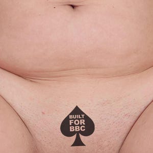 Puede incluir: Primer plano del torso de una persona, con un tatuaje negro de pica que dice "BUILT FOR BBC". El tono de piel es claro y la imagen se centra en la parte inferior del abdomen y el área púbica.