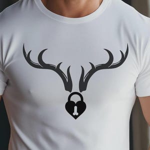 May include: White t-shirt featuring a black graphic of deer antlers above a heart-shaped padlock. The padlock design includes a stylized phallus. The shirt is made of a soft, white material.