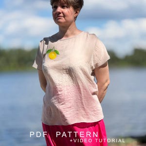 May include: A short-sleeved, beige-colored top featuring a small, embroidered yellow lemon with green leaves on the upper left chest. The garment has a round neckline and a textured fabric finish. The text "PDF PATTERN + VIDEO TUTORIAL" is visible.