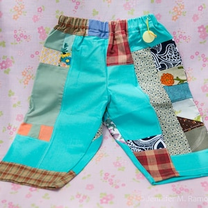May include: Patchwork pants featuring a bright turquoise base fabric accented with various fabric squares including red plaid, floral patterns, navy blue paisley, and solid orange. The pants have an elastic waistband and a small yellow tag.