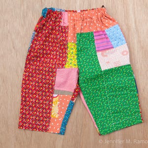 May include: Patchwork pants featuring an elastic waistband and a variety of colorful fabric panels. The garment displays a mix of floral, geometric, and solid patterns in shades of red, green, pink, orange, yellow, and blue, stitched together.
