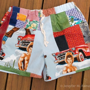 May include: Patchwork shorts with a light blue background featuring a cowboy and a red vintage car. The shorts have a drawstring waist and are made of various fabric patterns, including floral, plaid, and solid colors.